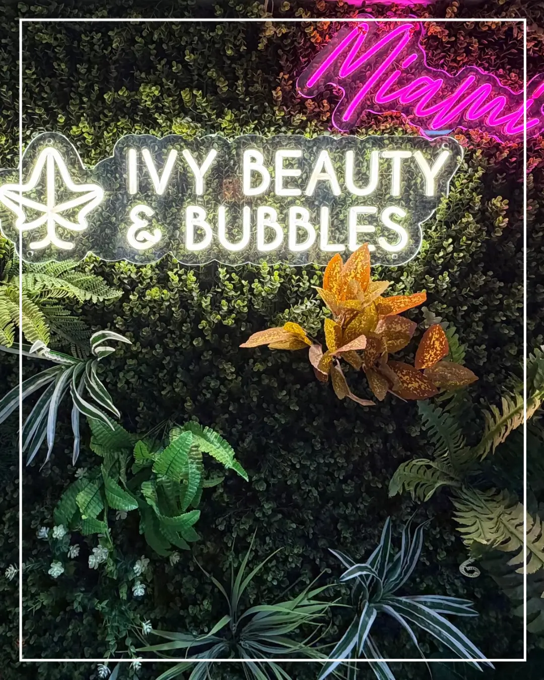 Plant wall with the illuminated IVY Beauty & Bubbles Doha salon sign.
